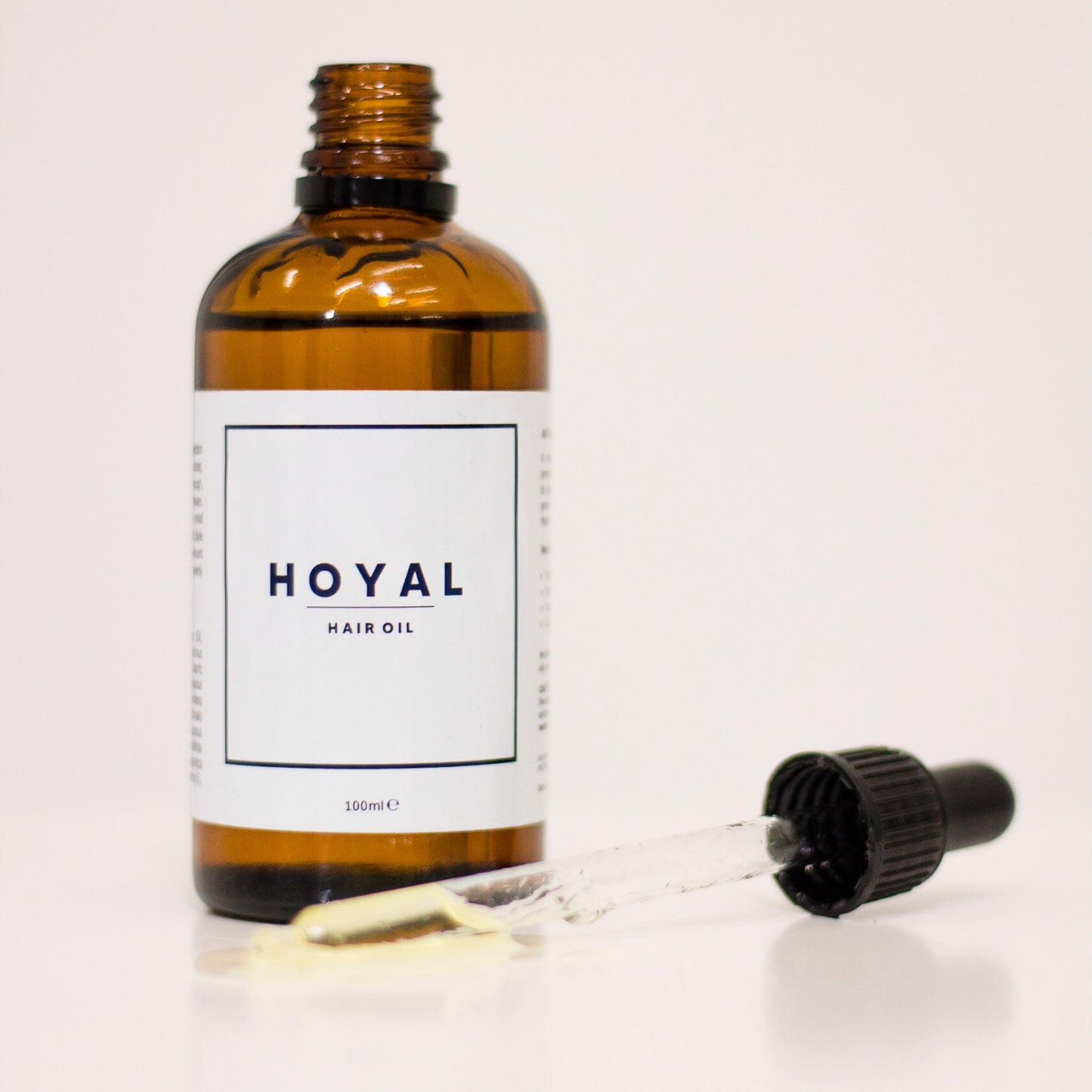 An open bottle of HOYAL Hair Oil beside a pipette with hair oil in it.